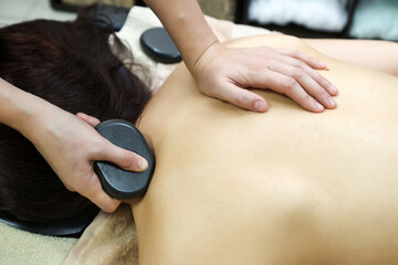 Effective modern hot stone massage of female back and neck, close-up.