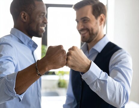 Spirit of friendly collaboration. Two male colleagues members of diverse multiethnic corporate workers group bump fists on informal team meeting in office celebrate achievements express mutual support