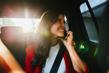 Smiling businesswoman talking on phone in car with sunlight streaming inside