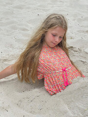 Beautiful girl buried in the sand on the beach