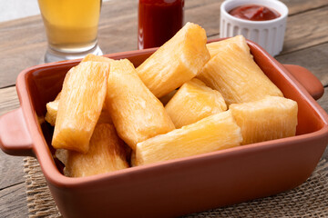 Traditional brazilian fried manioc in a plate with ketchup, pepper and beer over wooden table