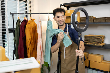 A man is selling clothes online, using his mobile phone. He is live selling with fun. He is smiling...