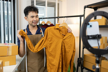 A man is selling clothes online, using his mobile phone. He is live selling with fun. He is smiling...