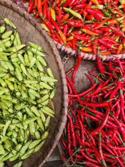 Colorful piles of fresh green and red chili peppers in woven baskets.