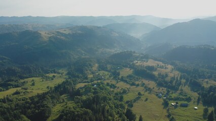 Obraz premium Aerial view of a fog creeping over the mountains surrounding the valley on a summer day.