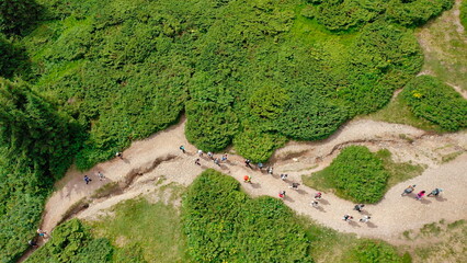A top-down aerial view of young people walking along a mountain trail to the top of the mountain.