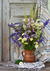 Still life with bouquet wild flowers in a clay jug on an old wooden background. Bouquet of colorful wildflowers