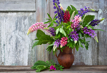 A bouquet of purple and pink lupine flowers in a clay jug on an old wooden background. Summer still...
