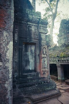 Temple entrance with an Apsara figure carved into stone, framed by decorative elements and shaded by trees.
