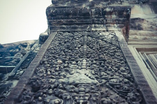 Upward view of a detailed stone pillar, adorned with floral patterns and ornate carvings from a Khmer temple wall.