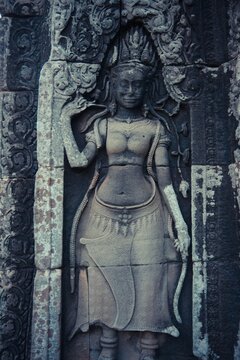 Close-up of an intricately carved Apsara dancer on an ancient temple wall, adorned with jewelry and surrounded by floral motifs. A stunning example of Khmer stone craftsmanship.