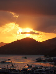The setting sun sinks behind Coron Island’s wooded hill, bathing Coron Bay in molten gold while...