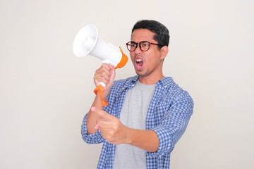 Adult Asian man showing angry face expression while protesting using megaphone
