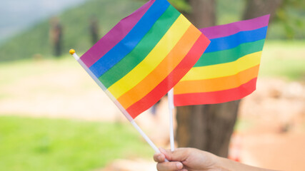 Two pride flags in hands. Concept of freedom, independence and diversity. Hand holding gay flags symbol of lgbtq outdoors on a bright space. identity pride