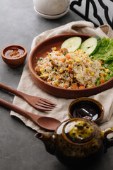 Indonesian Fried Rice (Nasi Goreng) with Vegetables, Chicken, and Egg – Served on Wooden Plate with Traditional Side Condiments, Colorful Asian Fried Rice Dish with Cucumber, Lettuce, and Condiments, 