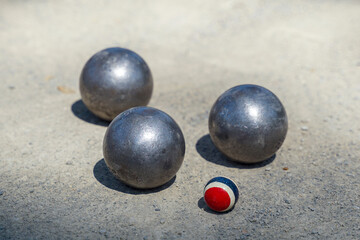 Petanque balls are placed near a target ball on an outdoor dirt field, where 12 round metal balls are thrown as close as possible to the target team that reaches 13. The first to score is the winner.