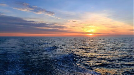 Fototapeta premium Vast sea with setting sun shining on endless water surface, blue sky with white clouds on the horizon, and ripples rising from deep ocean bottom, forming a magnificent natural landscape.