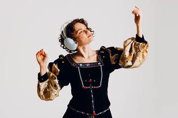 Young adult woman with headphones on her head and dressed in a medieval dress listens music...