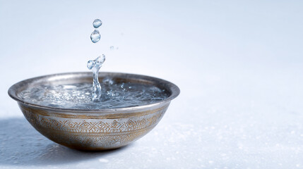 Water droplets splash in antique silver bowl filled with clear water. Bright setting emphasizes tranquility and calmness. Concept of wellness, spa, meditation