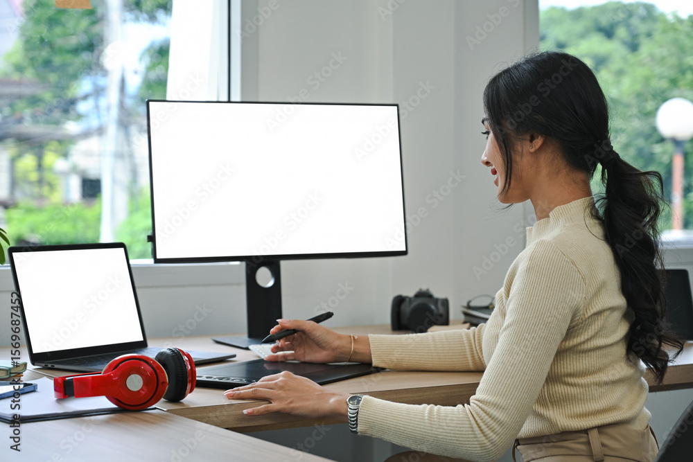 Fototapete Creative designer focused on her project using a graphic tablet and dual monitors. Bright workspace with a contemporary setup and an inspiring atmosphere
