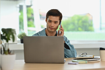 Fototapeta premium A Young Asian businessman multitasking with a phone call and laptop