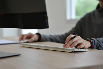 Close-up view of a professional’s hands typing on a keyboard and using a mouse while working on a...