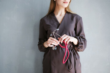 Close-up of female healthcare professional in medical uniform holding red stethoscope against gray wall.