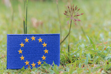 Eco friendly embroidered European Union flag on green grass with wildflowers. Natural light , ...
