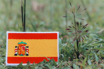 Eco friendly embroidered Spanish flag on fresh green grass with wildflowers. Horizontal photo in...