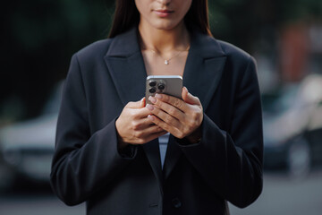 Hands of business woman using smartphone at city street