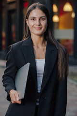 Woman in business suit holding laptop at the city