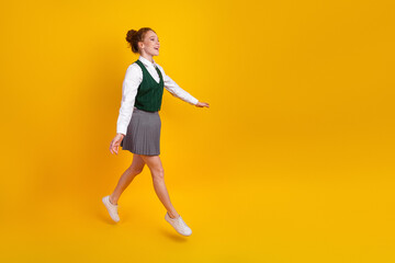 Cheerful student walking confidently in school uniform against yellow background