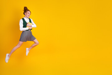 Energetic schoolgirl jumping joyfully in a stylish uniform while holding books against a vibrant...
