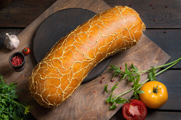 Beautiful meat sausage on a wooden table among greens, vegetables and spices