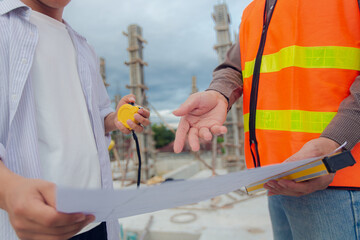 Construction contractor discussing, checking and recording construction work using computer, tape measure, spirit level and wearing yellow construction equipment. House construction concept.