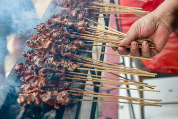 Grilling Meat Skewers Over Charcoal with Hand Holding Some