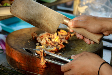 Preparing Grilled Food with Cleaver and Tongs on Round Wooden Board