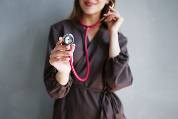 Close-up of female hand holding red stethoscope toward camera, doctor wearing dark medical uniform.