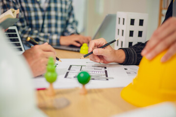 Engineers and architects discuss and consider construction plans for new renewable energy project in office with design documents, laptop and hard hat on table. Concept of engineers and architects+