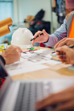 Engineers and architects discuss and consider construction plans for new renewable energy project in office with design documents, laptop and hard hat on table. Concept of engineers and architects+