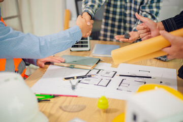 Engineers and architects discuss and consider construction plans for new renewable energy project in office with design documents, laptop and hard hat on table. Concept of engineers and architects+