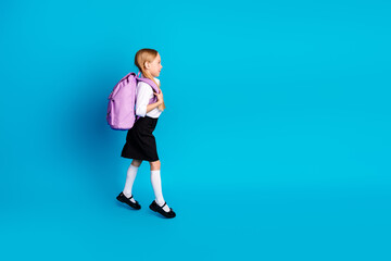 Cute schoolgirl walking with backpack on blue backdrop, showcasing school readiness, education...