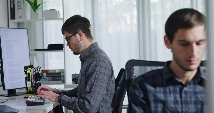 Adult male engineer team discusses AI software development robotic hand project use AI code solutions at tech workspace. Artificial intelligence interface, collaboration support prototype development.