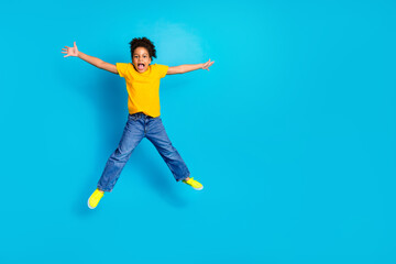 Obraz premium Cheerful young child in vibrant yellow shirt leaping joyfully against a bright blue backdrop full of energy