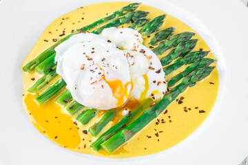 White Plate of Asparagus Nestled in Hollandaise Sauce With Poached Egg