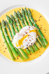 White Plate of Asparagus Nestled in Hollandaise Sauce With Poached Egg