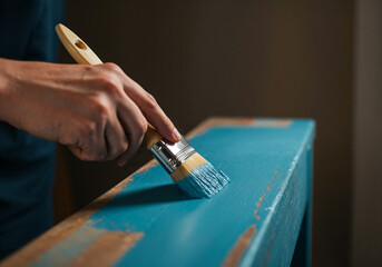 Close-up of a hand painting vintage wooden furniture with light blue brush-on paint