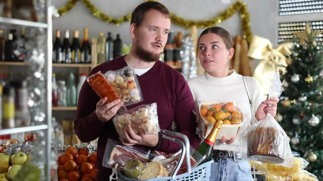 Joyful husband and wife choose and buy nougat, panettone, marzipan, panellets together in grocery department of supermarket
