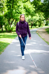 Visually impaired woman with white cane walking in the city park