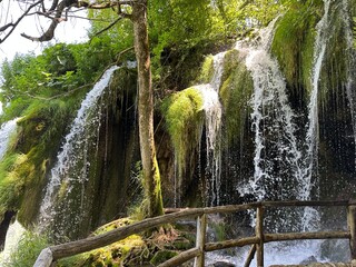 The beautiful waterfall in Plitvice Lakes, Croatia, flows gracefully through summertime greenery and majestic mountains, offering an exquisite sanctuary for nature enthusiasts and outdoor lovers.